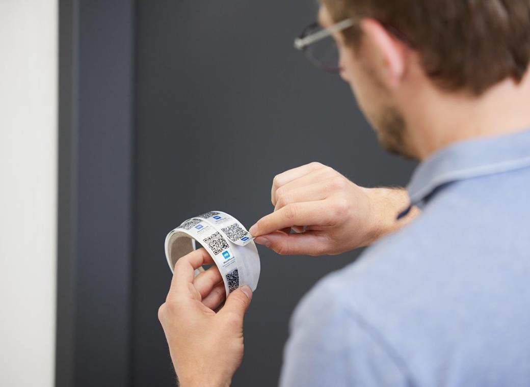 Ein Mitarbeiter zieht die effiziente Kennzeichnungslösung mit QR-Code von der Rolle ab zur Verklebung.