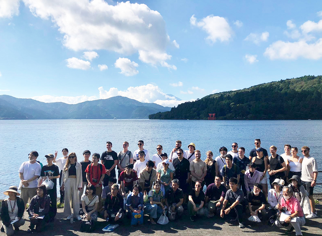 Group picture of Master students at Lake Ashi with gate and Mount Fuji in the background hidden by the clouds.