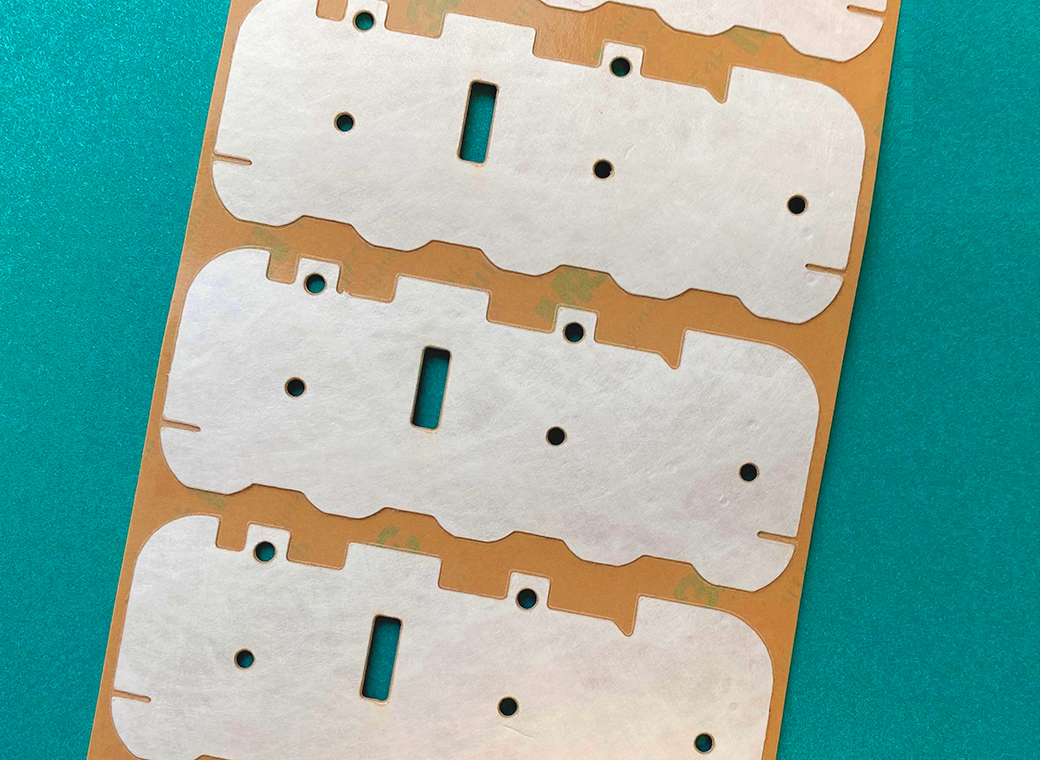 The self-adhesive blanked part has an unusual shape and several small cut-outs that are also punched through the liner.